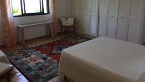 Une chambre à coucher comprenant un lit, un bureau, une chaise, un tapis à motifs et une armoire.