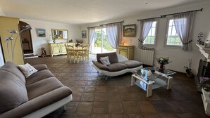 A spacious living area with a sofa, a chair, a dining table, and a kitchen in the background. - Architect-designed house with swimming pool, near the sea, 6 adults / 2 children (Draguignan)