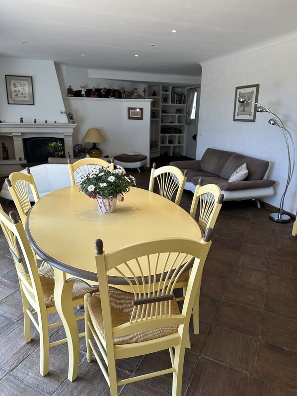 A dining area with a round table and six chairs, a sofa, a bookshelf, and a floor lamp.