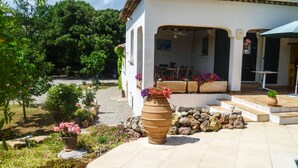 A white building with a tiled roof, outdoor seating area, and a garden with potted plants and flowers. - Architect-designed house with swimming pool, near the sea, 6 adults / 2 children (Draguignan)
