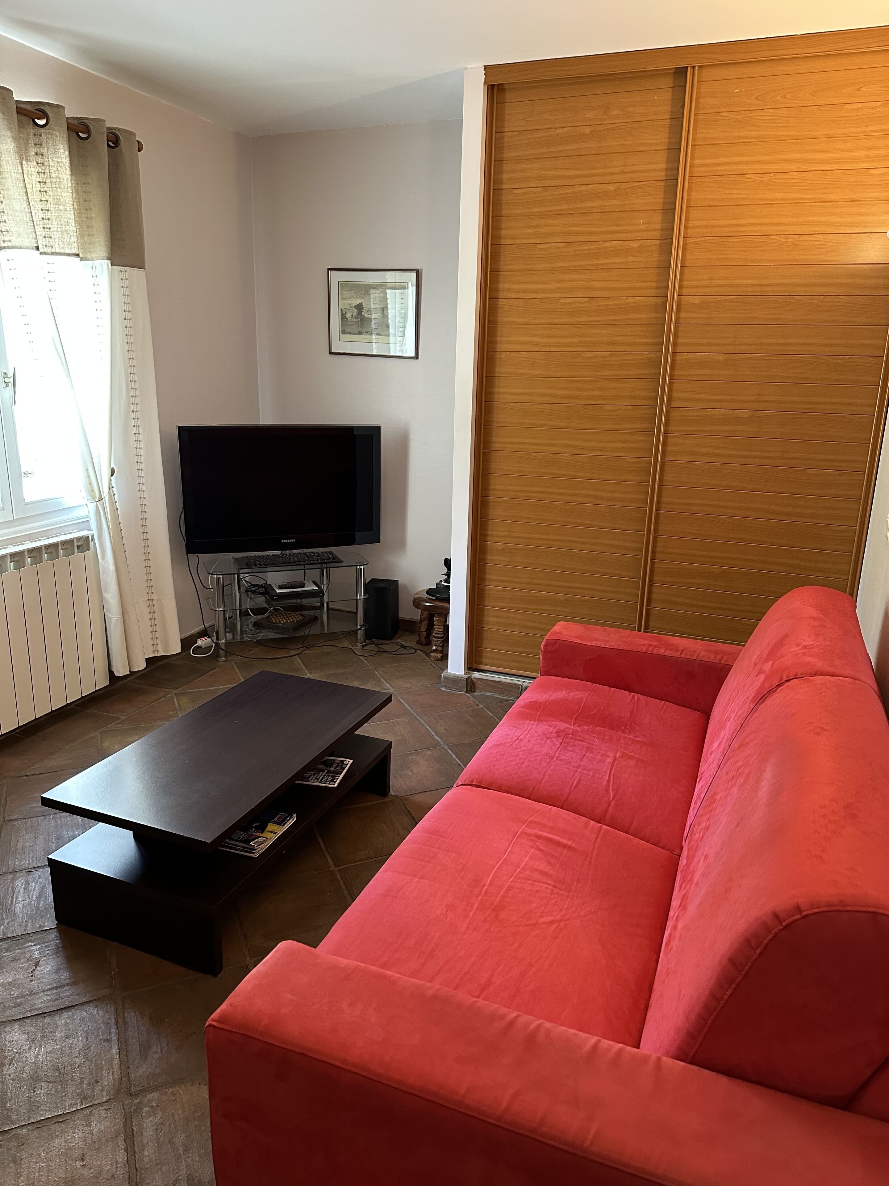 A living room with a red sofa, a black coffee table, a TV on a stand, and a wooden sliding door.