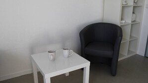 Mesa branca com duas canecas e uma poltrona escura em um quarto com paredes e estantes brancas.