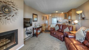 A living room with a fireplace, a leather sofa, a dining area, and a kitchen with wooden cabinets.