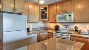 A kitchen with wooden cabinets, a white refrigerator, a microwave, an oven, and granite countertops.