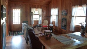 A wooden cabin interior with a sofa, a dining table, a fireplace, and a ceiling fan.