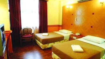 A hotel room with two single beds, a wooden headboard, a chair, a desk, and a window with curtains.