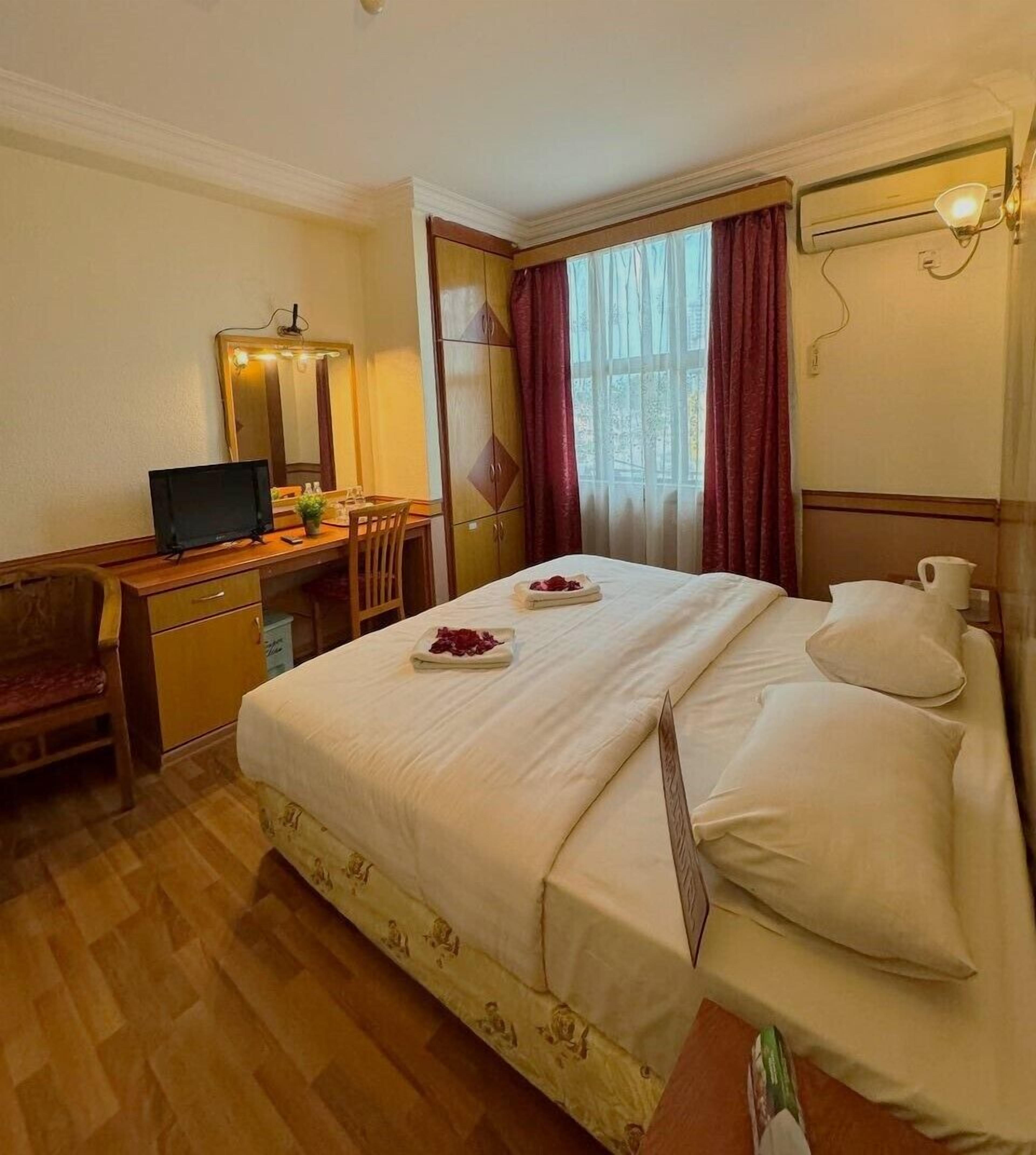 Una habitación de hotel con cama, escritorio con computadora, silla, espejo y ventana con cortinas.