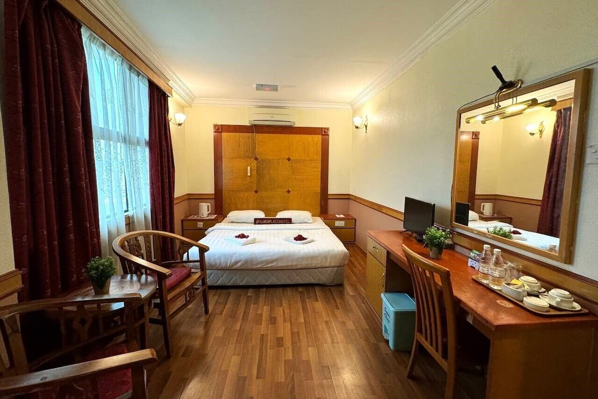 Quarto de hotel com uma cama, uma escrivaninha, uma cadeira, um espelho e uma pequena mesa com uma bandeja de objetos.
