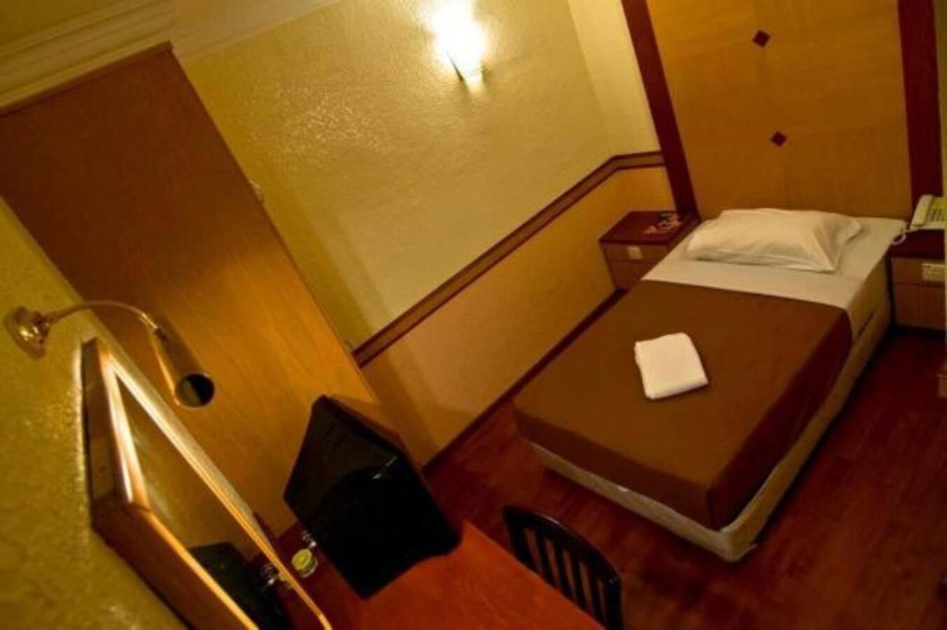 A small hotel room with a single bed, a chair, a desk, and a mirror.