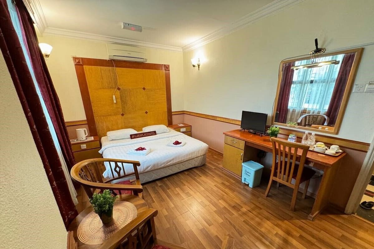 Quarto de hotel com cama, escrivaninha, cadeira e uma pequena mesa com uma planta.