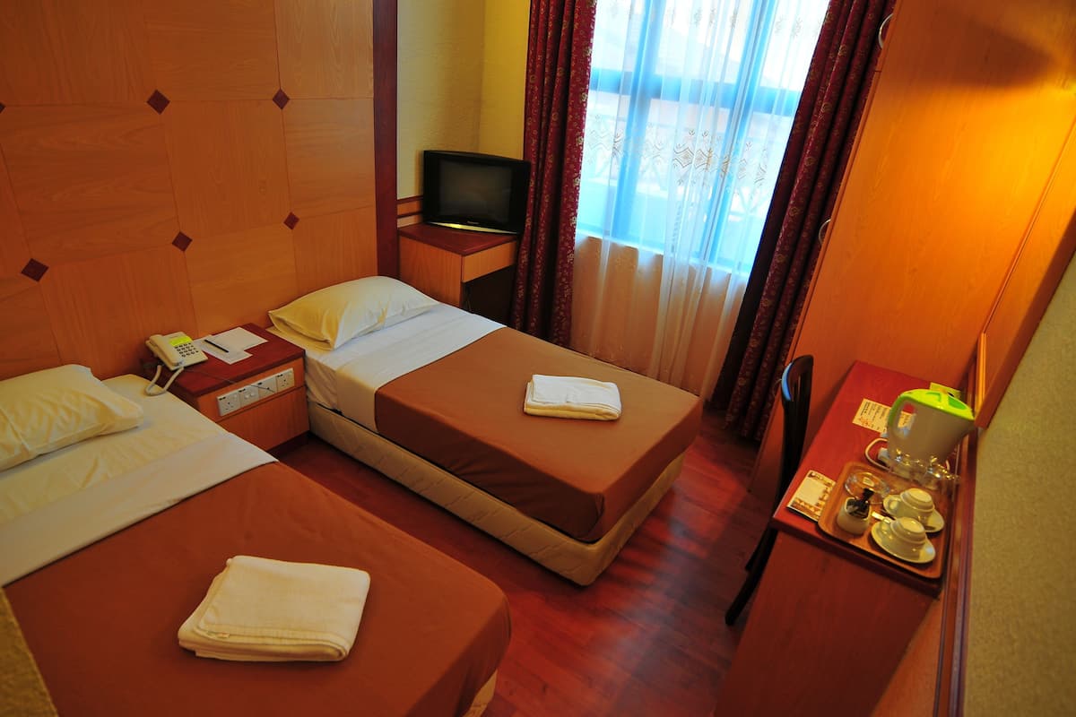 Quarto de hotel com duas camas, uma escrivaninha com telefone e papéis, uma televisão e uma janela com cortinas.