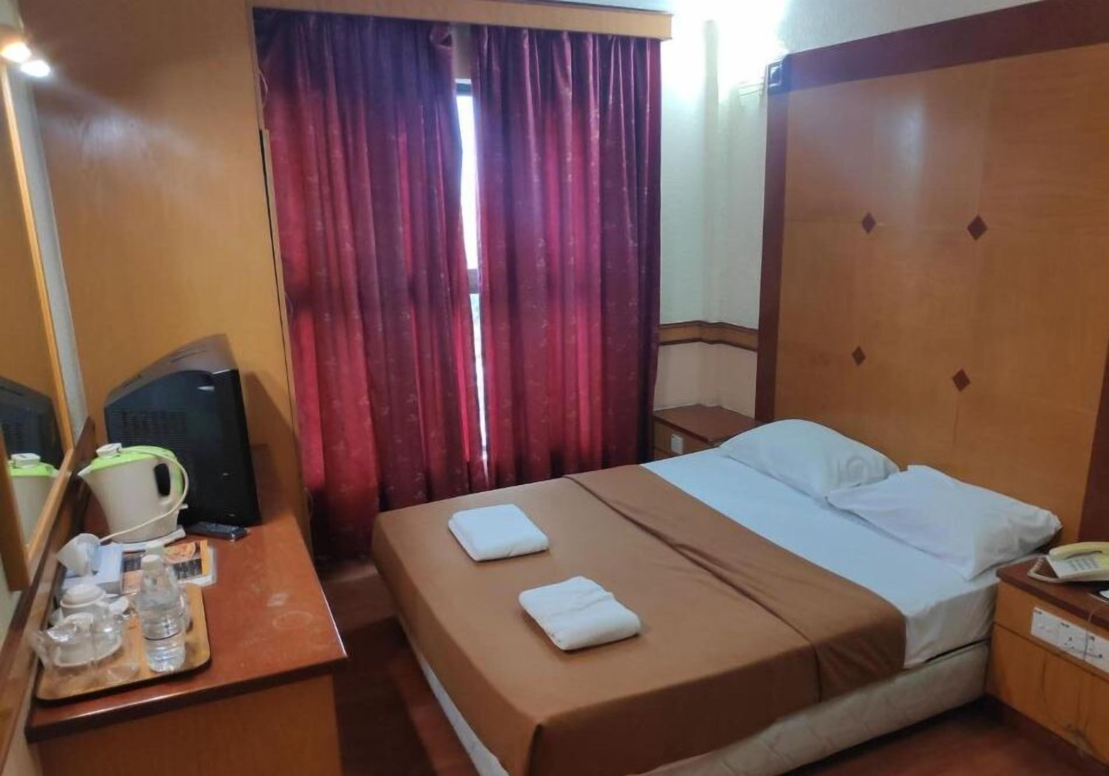 A hotel room with a bed, a desk with a kettle, a telephone, and a window with curtains.