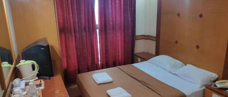 Habitación de hotel con cama, escritorio con tetera, teléfono y ventana con cortinas.