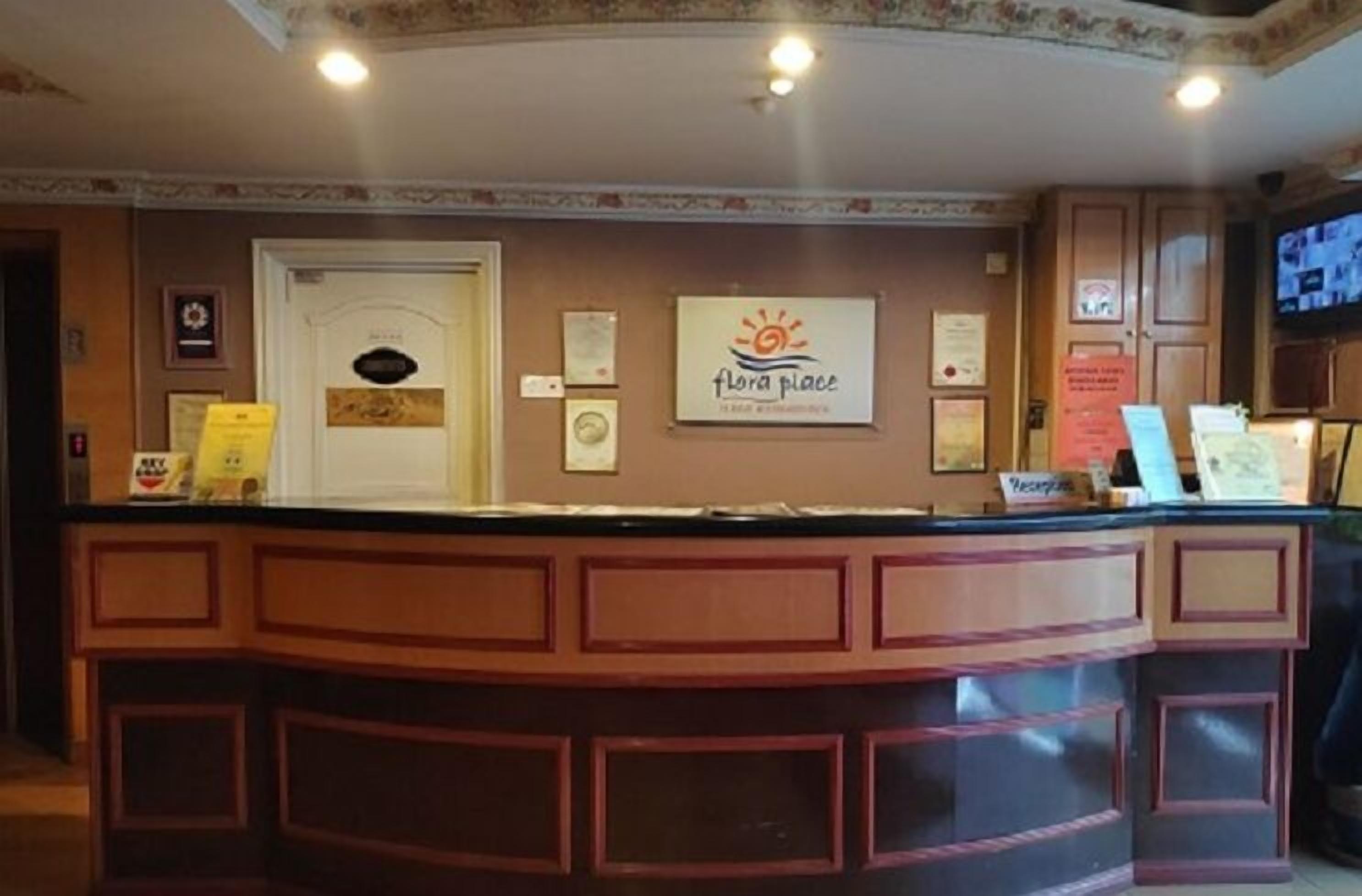 A reception desk with a sign reading "flora place" and a television screen mounted on the wall.