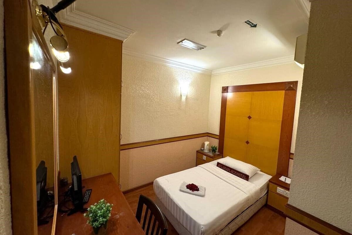 Quarto de hotel com cama, escrivaninha com computador, uma pequena planta e um espelho.