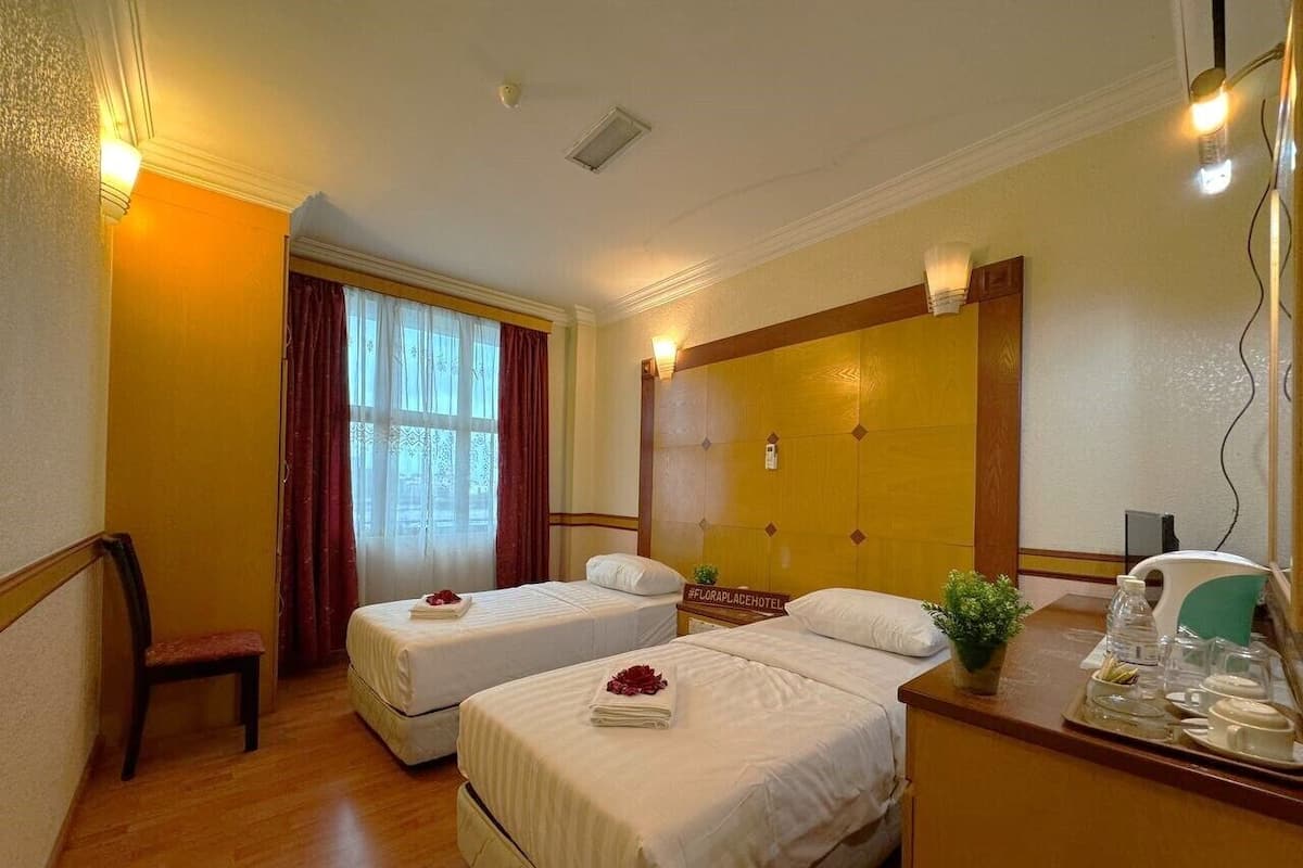 Quarto de hotel com duas camas, uma escrivaninha de madeira, uma cadeira, uma janela com cortinas e um letreiro na parede.