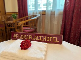 Un letrero de hotel con el hashtag #FLORAPPLACEHOTEL, una toalla blanca y una rosa roja sobre una cama.