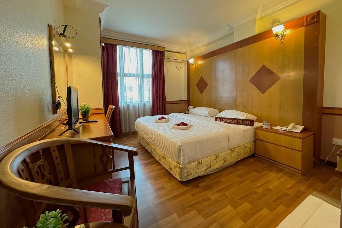 Quarto de hotel com cama, escrivaninha, cadeira e uma pequena mesa com uma planta.