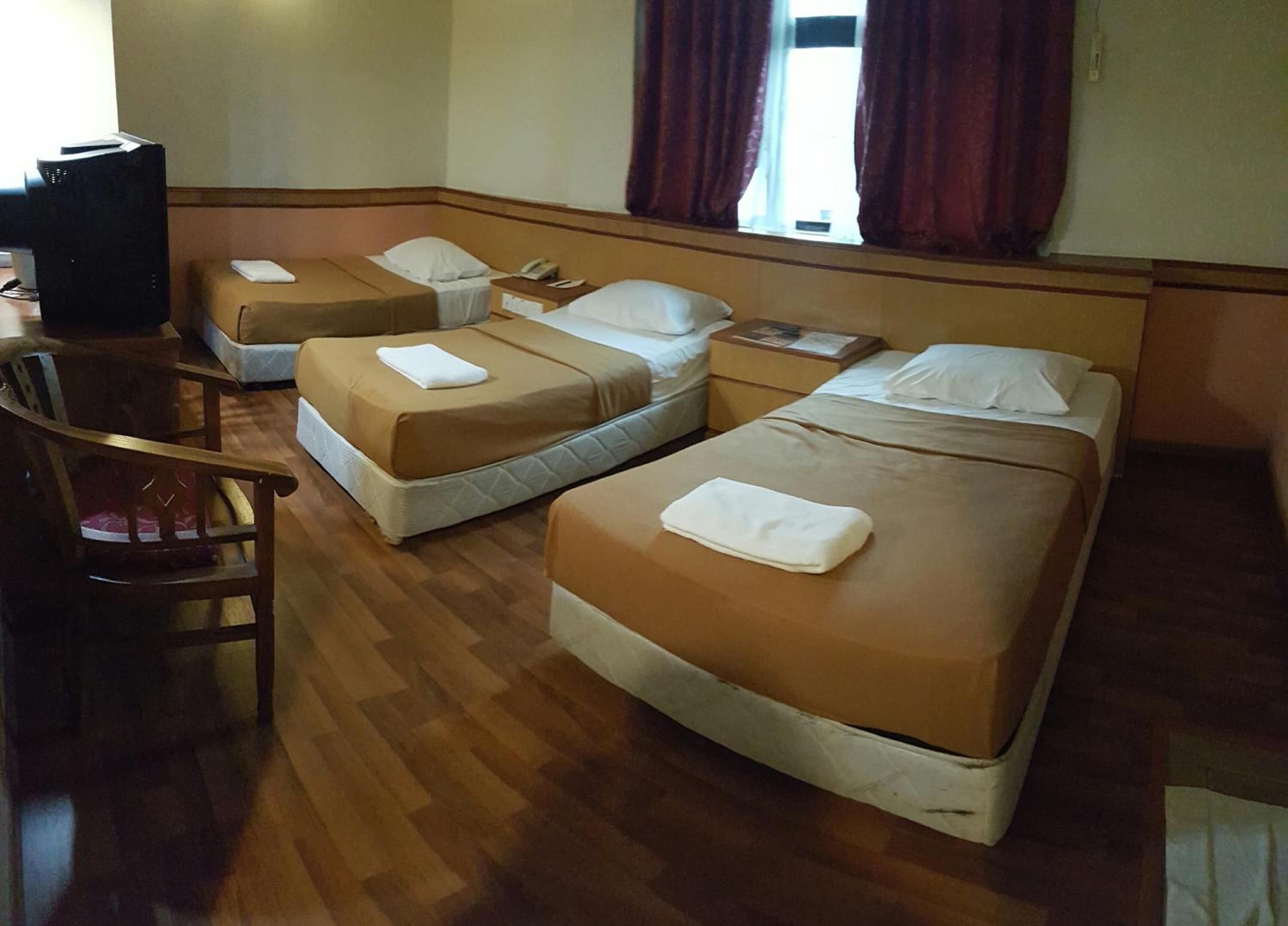 Una habitación de hotel con tres camas individuales, una silla de madera y un escritorio con una computadora.