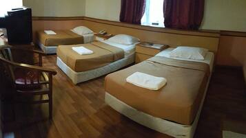 Una habitación de hotel con tres camas individuales, una silla de madera y un escritorio con una computadora.