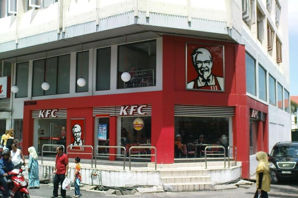 Ein KFC Restaurant mit roter Außenfassade, großen Fenstern und einer sichtbaren Durchfahrt für Autofahrer.