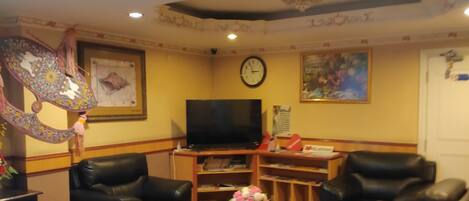 A living room with black leather sofas, a flat-screen TV, a clock, and a floral arrangement on a wooden coffee table.