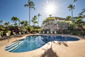 Une piscine avec des chaises longues, des palmiers et un bâtiment en arrière-plan.