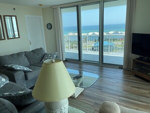 Un salón con sofá, lámpara, televisor y un ventanal con vistas al mar y edificios.