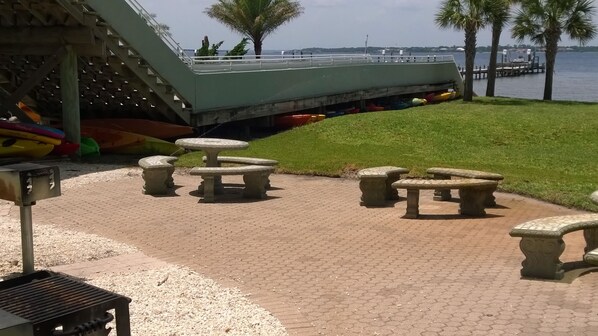 Un patio empedrado con bancos de piedra y una zona de barbacoa, con vistas a un cuerpo de agua y un muelle.