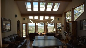A spacious living room with a ping pong table, leather sofas, and large windows offering a view of the outdoors.