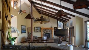 A spacious living area with a stone fireplace, wooden beams, a large TV, and a dining area with a stone countertop and sink.