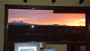 A room with a large window overlooking a mountain range at sunset.