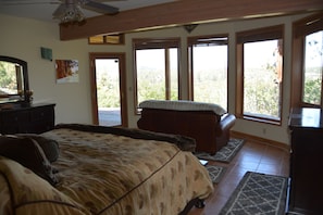 A bedroom with a large bed, a dresser, and a window with a view of trees.