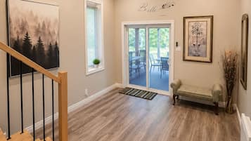 A modern interior with a wooden staircase, a dining area with outdoor patio access, and a wall-mounted artwork.