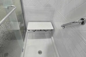 Un espace douche avec un banc blanc, une porte en verre et un mur carrelé.