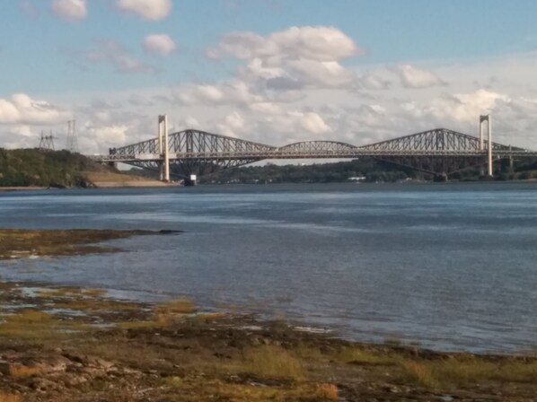 Un grand pont d’acier enjambant une large rivière, avec un ciel dégagé au-dessus.