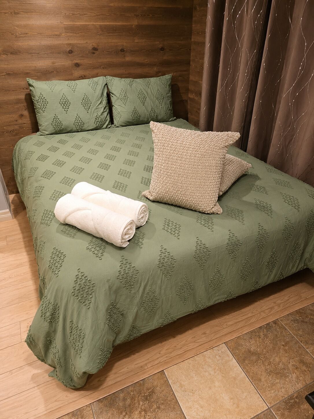 Un lit recouvert d’une couvre-lit à motifs verts, avec deux oreillers et une serviette blanche enroulée.