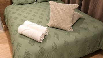 Un lit recouvert d’une couvre-lit à motifs verts, avec deux oreillers et une serviette blanche enroulée.