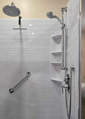 Un espace douche moderne équipé d’un pommeau de douche à main, d’un pommeau de douche fixe et d’un flexible de douche à main.