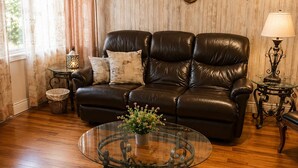 A living room with a leather sofa, a glass coffee table with a plant, a wall-mounted bull skull decoration, and a lamp on a side table.