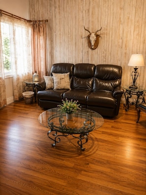 Un salon avec un canapé en cuir, une table basse en verre ornée d’une plante, une décoration murale représentant un crâne de taureau et une lampe posée sur une table d’appoint.