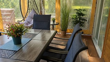 A covered patio with a table and chairs, a hanging chair, and potted plants.