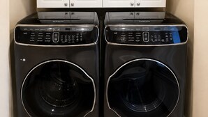 Two black front-loading washing machines with control panels, placed in a corner with a white cabinet above them.