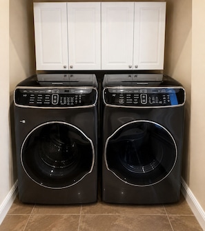 Deux machines à laver à chargement frontal de couleur noire, dotées de panneaux de commande, sont placées dans un coin, avec un meuble blanc au-dessus.