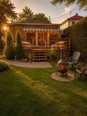 En baghave med træterrasse, bålsted, udendørs møbler og et juletræ.