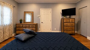 A bedroom with a bed, two wooden dressers, a television, a door, and a ceiling fan.