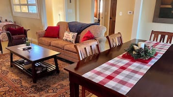 Ein gemütliches Wohnzimmer mit einem gemusterten Sofa, einem Holztisch und einem Esstisch mit kariertem Tischläufer.