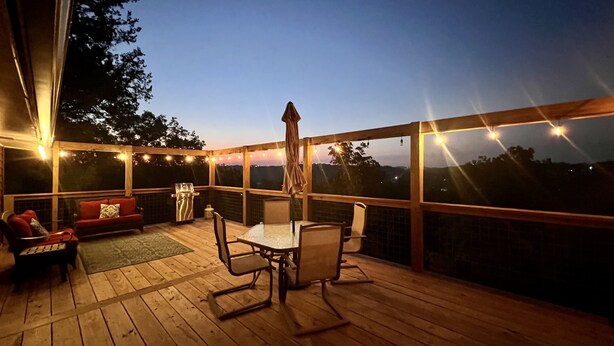 Una terraza de madera con una mesa, sillas, una parrilla y luces colgantes.