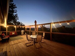 A wooden deck with a table and chairs, a grill, and string lights.