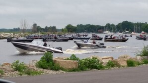 Un port de plaisance où de nombreux bateaux sont amarrés et en mouvement, entouré d’une côte rocheuse et de verdure.